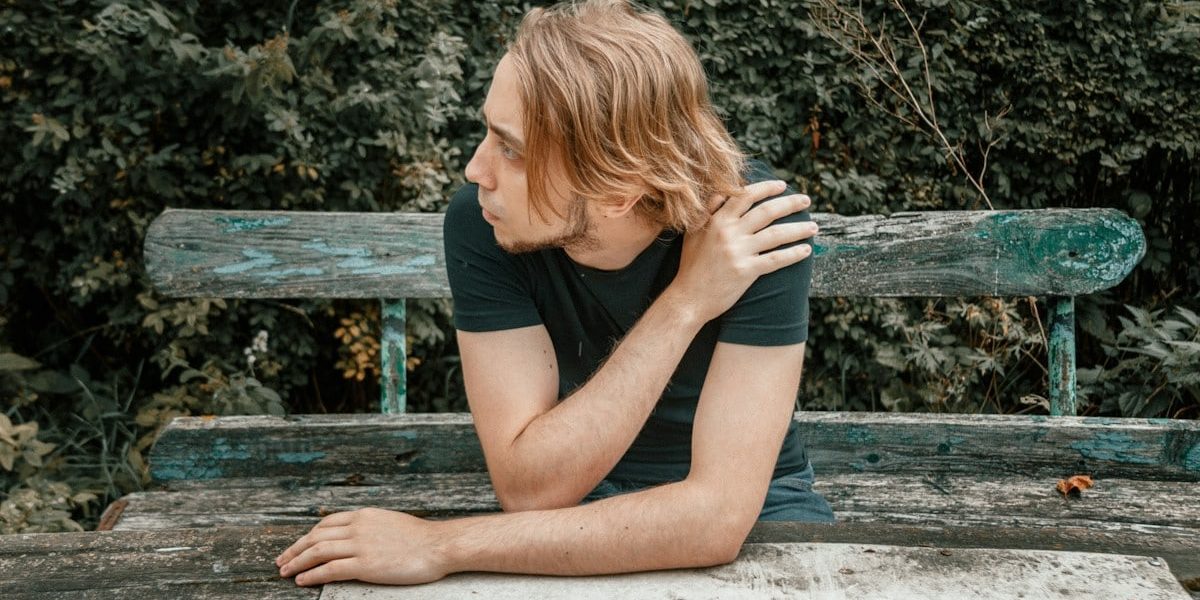 a man sitting on a wooden bench in front of a bush