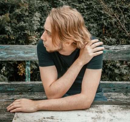 a man sitting on a wooden bench in front of a bush