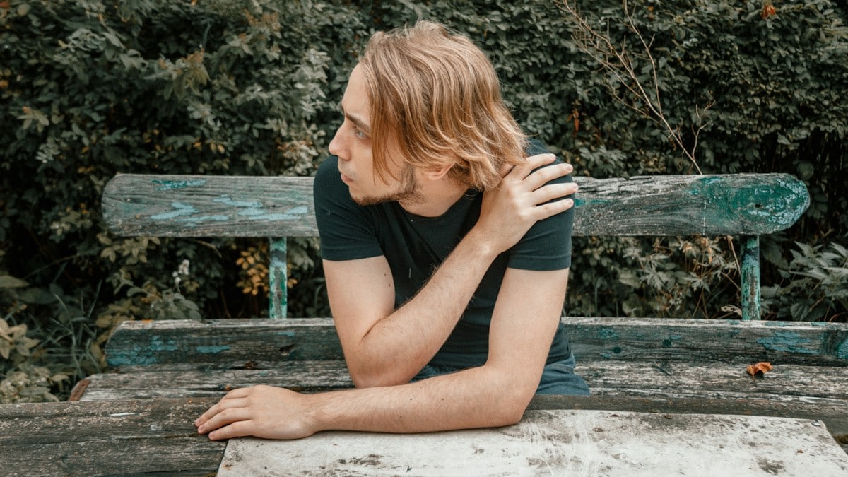 a man sitting on a wooden bench in front of a bush
